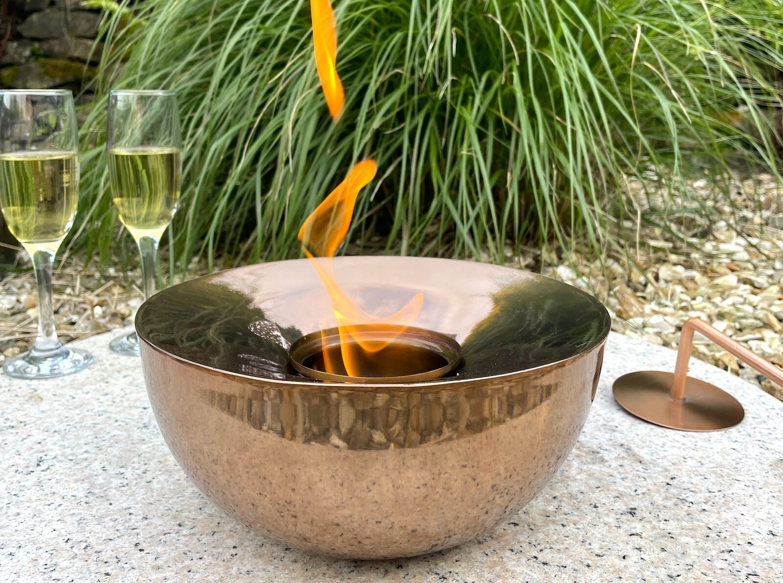 Copper gel lamp with flame in garden in front of grass and next to drinks