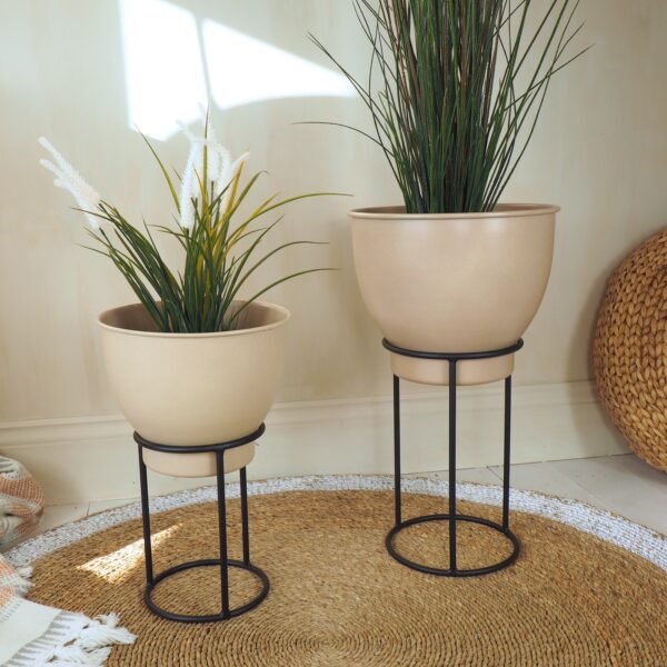 Two beige metal plant stands on wicker rug with plants